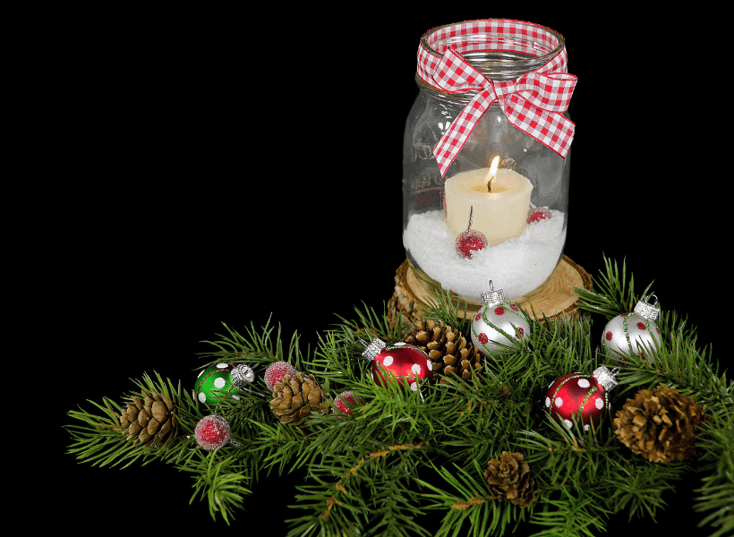 Decorated mason jar on a wood block with artificial Christmas tree branch and baubles around it